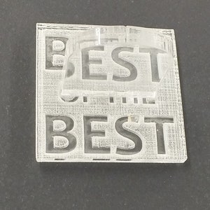 以下が含まれることがあります： 表面に「BEST」の文字が刻まれた透明アクリルパズル。パズルは2つのパーツで構成されており、ベースには「BEST」の文字が繰り返されています。シンプルでモダンなデザインです。
