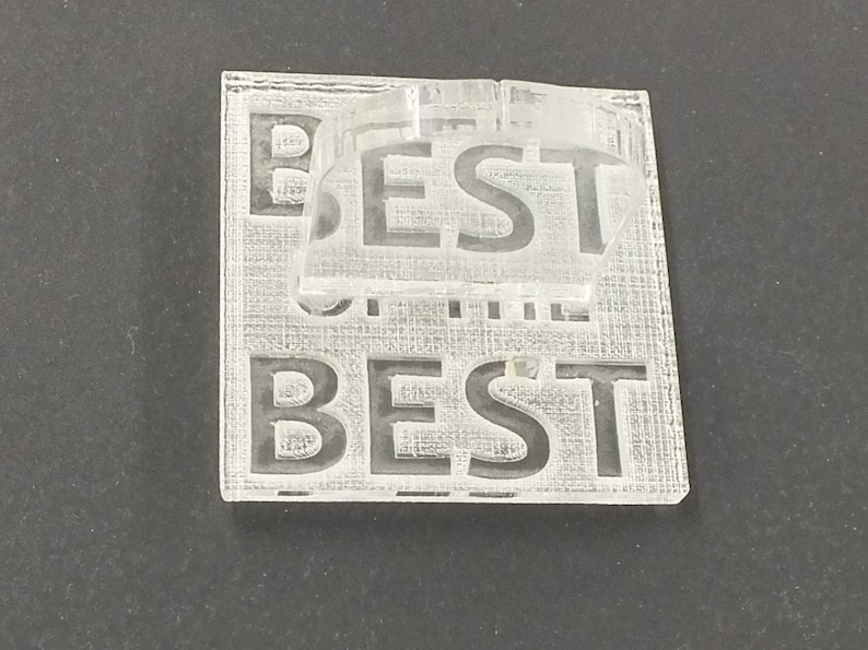 以下が含まれることがあります： 表面に「BEST」の文字が刻まれた透明アクリルパズル。パズルは2つのパーツで構成されており、ベースには「BEST」の文字が繰り返されています。シンプルでモダンなデザインです。