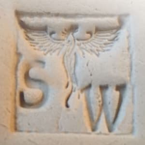 以下が含まれることがあります： オフホワイトの正方形のレリーフ彫刻で、「S」と「W」の文字が、様式化された翼のある生き物を挟んでいます。 生き物は翼を広げ、流れるような尾を持ち、すべてがくぼんだ境界線の中にあります。