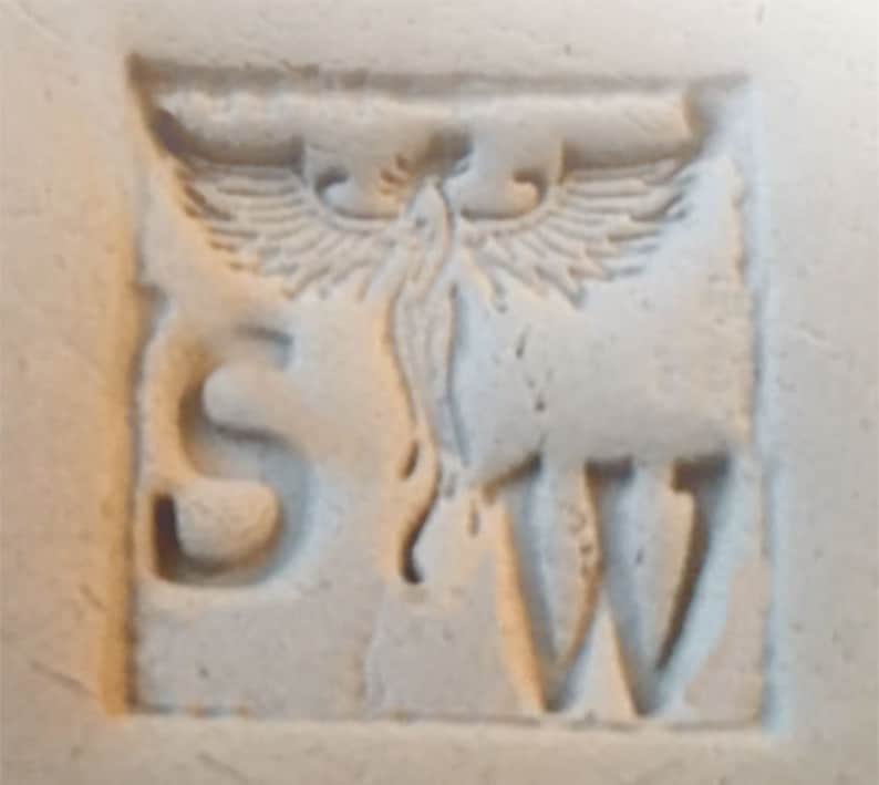 以下が含まれることがあります： オフホワイトの正方形のレリーフ彫刻で、「S」と「W」の文字が、様式化された翼のある生き物を挟んでいます。 生き物は翼を広げ、流れるような尾を持ち、すべてがくぼんだ境界線の中にあります。