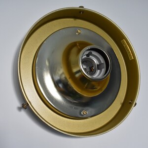 May include: A gold-colored ceiling light fixture with a central silver-colored bulb socket. The fixture has a circular design with a brass-colored outer ring and is mounted on a white surface.
