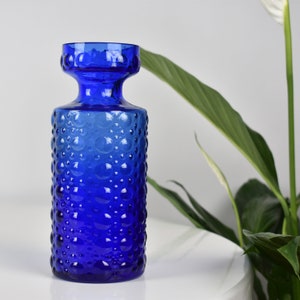 Peut inclure: Un vase en verre bleu cobalt avec un motif texturé de bulles. Le vase a une large ouverture et un col étroit.