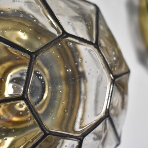 May include: Close-up of two geometric glass objects with a metallic finish. The objects have a multifaceted design with black outlines. The glass has a reflective surface with small bubbles, and the interior has a golden hue.