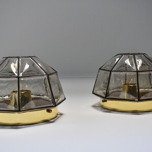May include: Two vintage, geometric-shaped lamps with clear, textured glass shades and brass-colored bases. The shades are multi-faceted, and the lamps are designed to sit on a surface. The lamps are likely for home decor.