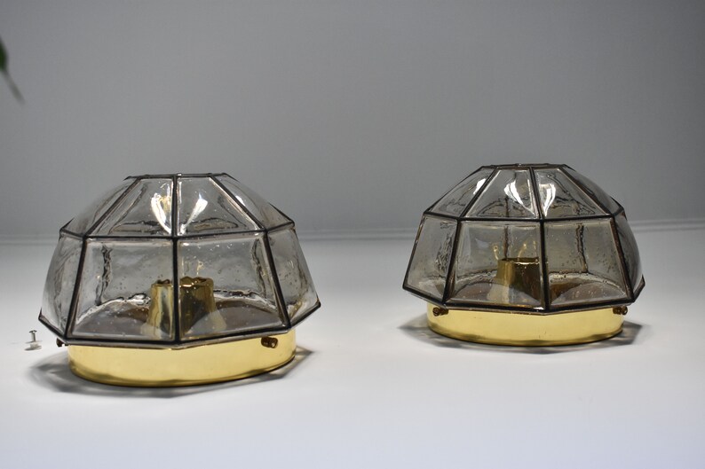 May include: Two vintage, geometric-shaped lamps with clear, textured glass shades and brass-colored bases. The shades are multi-faceted, and the lamps are designed to sit on a surface. The lamps are likely for home decor.