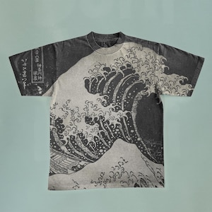 Puede incluir: Una camiseta negra con una gran impresión blanca de una ola. La ola es un diseño japonés tradicional, y la camiseta tiene texto japonés en la manga.