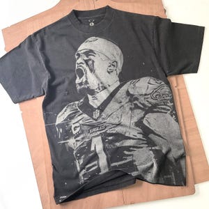 Op de afbeelding: Zwart T-shirt met een witte grafische print van een voetballer die een shirt draagt met nummer "1" en het woord "EAGLES".
