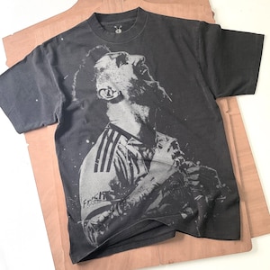 Puede incluir: Camiseta gris oscuro con una imagen en escala de grises de un jugador de fútbol mirando hacia arriba. La camiseta tiene cuello redondo y mangas cortas. La camiseta del jugador tiene el logo de Adidas y el texto "Frich Otto".