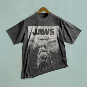 May include: A black t-shirt with a vintage-style graphic of a shark's mouth with the word "JAWS" printed above it.