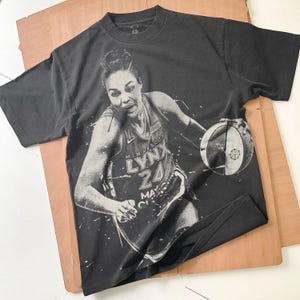 May include: Black t-shirt featuring a grayscale image of a basketball player in action, holding a basketball. The player is wearing a jersey with "MINNESOTA LYNX" and the number "24". The shirt has a vintage, worn look.