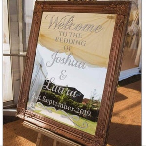 May include: A gold-framed mirror with a white inscription that reads "Welcome to the wedding of Joshua & Laura 21st September 2019".