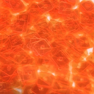 Peut inclure: Une image en gros plan d'un tas de carrés en plastique orange. Les carrés sont translucides et ont un léger éclat. Les carrés sont disposés de manière aléatoire.