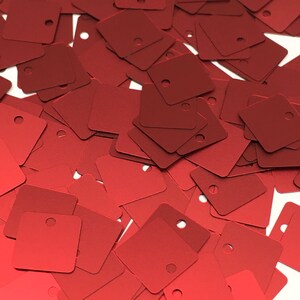 May include: A pile of red square sequins with a hole in the centre of each sequin.