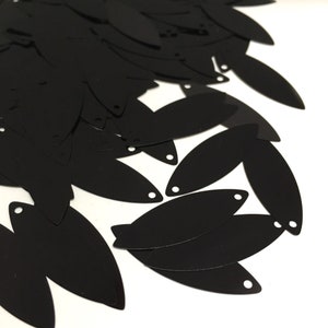 May include: A pile of black oval sequins with a hole in the centre of each sequin.