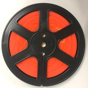 May include: A black plastic reel with orange thread wound around it. The reel has a label that says "Studio".