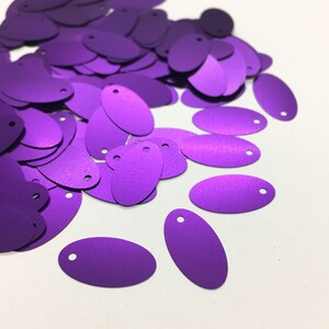 Puede incluir: Un montón de lentejuelas ovaladas de color púrpura con un agujero en el centro de cada lentejuela.