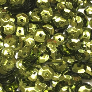 May include: A close-up image of a pile of green sequins. The sequins are shiny and have a faceted design.