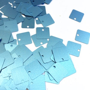 May include: A pile of light blue square sequins with a hole in the center of each sequin.