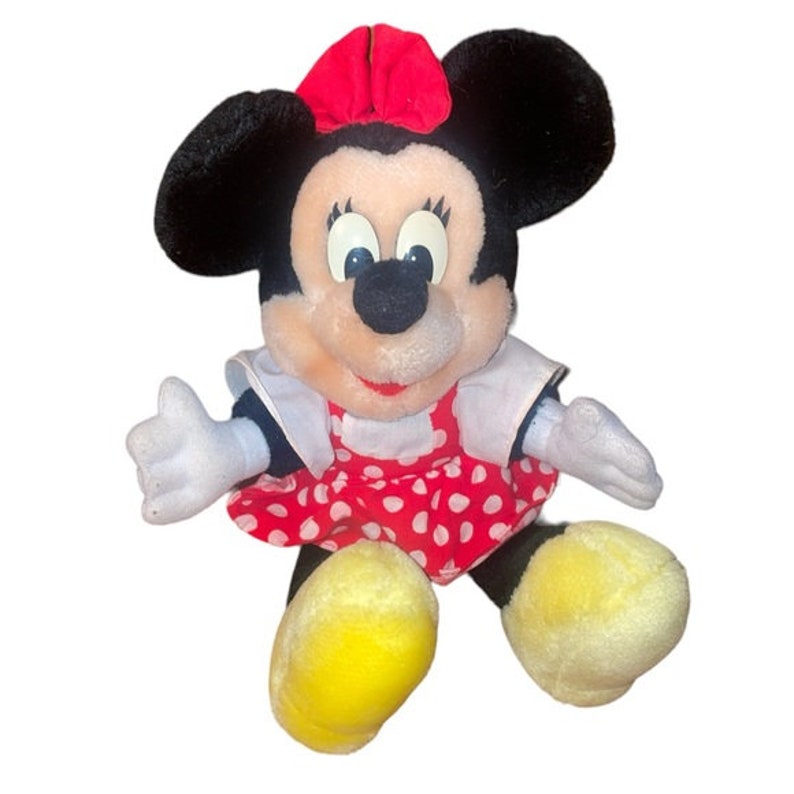 May include: A plush toy of Minnie Mouse wearing a red dress with white polka dots and a red bow. She has black ears and a black nose.