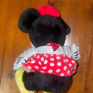 May include: A plush toy of Minnie Mouse wearing a red and white polka dot dress with a red bow on her head.