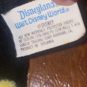 May include: A white tag with black text that reads "Disneyland Walt Disney World" and "DISNEY" with additional information about the product's materials and origin.
