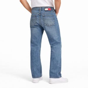 May include: Light blue denim jeans with a classic five-pocket design. The jeans feature a straight leg cut and a small red, white, and blue logo patch on the back pocket. The jeans are worn with white sneakers.