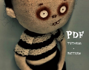 May include: A handmade rag doll with black hair, a striped shirt, and black shorts. The doll has a painted face with large eyes and a wide smile. The image includes the text "PDF TUTORIAL + PATTERN".