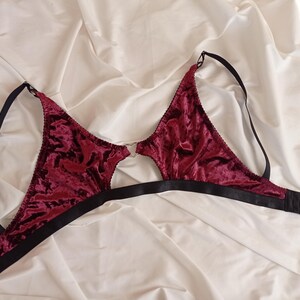 May include: A burgundy velvet bra with black adjustable straps and a hook closure in the back. The bra has a cut-out design in the front.