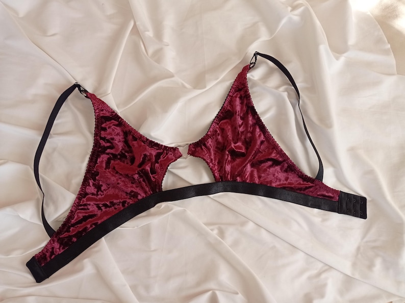 May include: A burgundy velvet bra with black adjustable straps and a hook closure in the back. The bra has a cut-out design in the front.