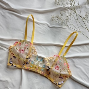 May include: A yellow floral lace bralette with adjustable straps. The bralette is made of a sheer fabric with delicate embroidery of colourful flowers and leaves.