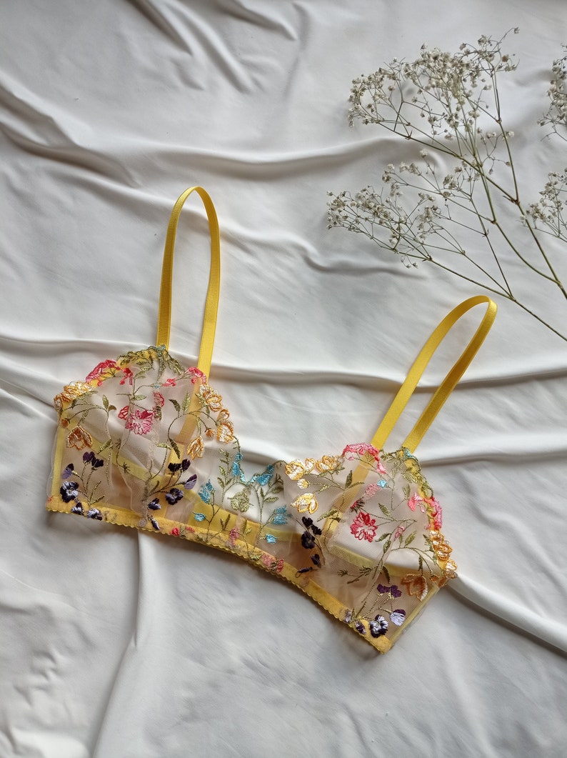 May include: A yellow floral lace bralette with adjustable straps. The bralette is made of a sheer fabric with delicate embroidery of colourful flowers and leaves.