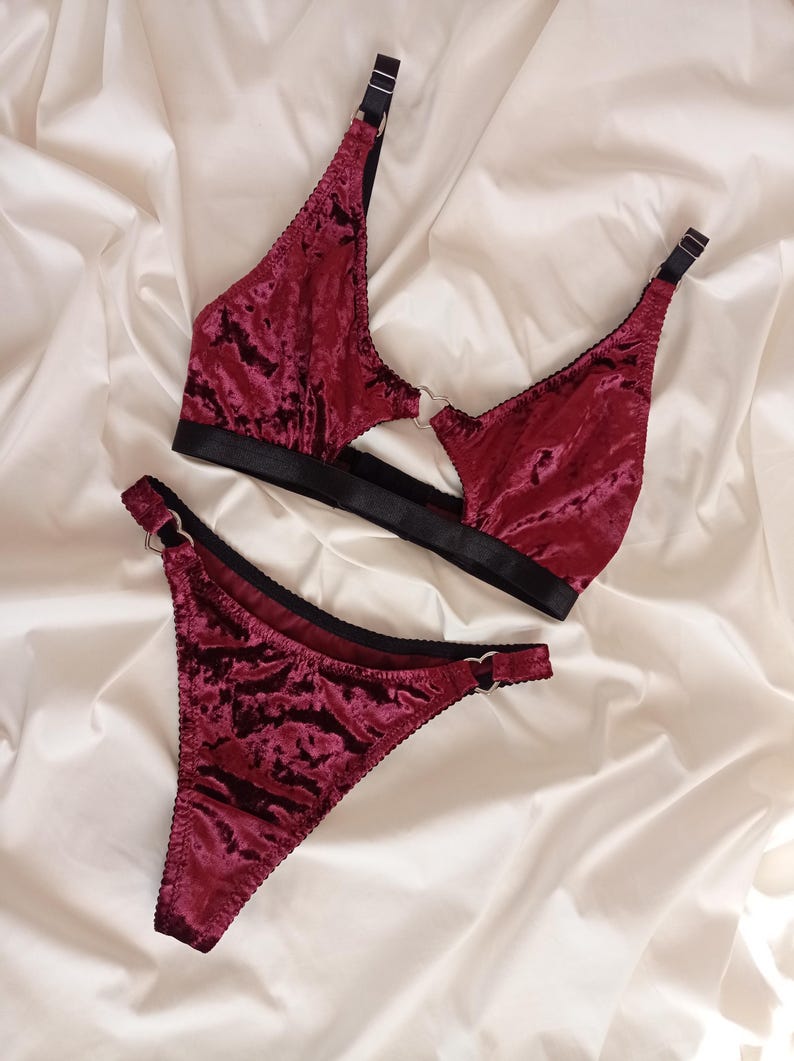 May include: A burgundy velvet lingerie set with black trim and silver rings. The set includes a bra and a thong.