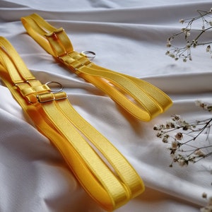 May include: Two yellow adjustable straps with silver metal rings and buckles. The straps are made of a soft, silky material.
