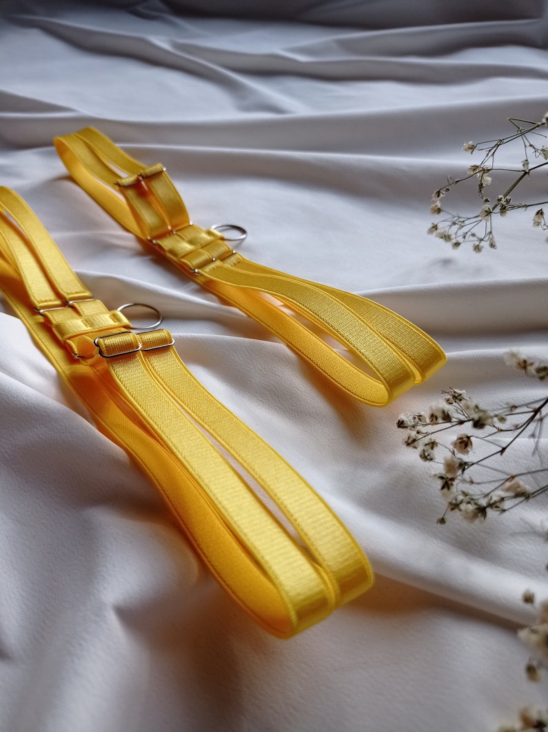 May include: Two yellow adjustable straps with silver metal rings and buckles. The straps are made of a soft, silky material.