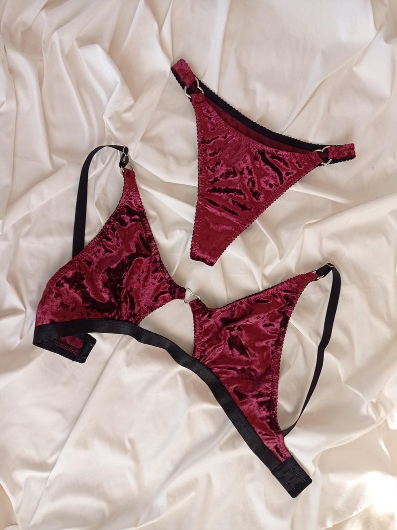 May include: A burgundy velvet lingerie set with black trim and silver rings. The set includes a bra and a thong.