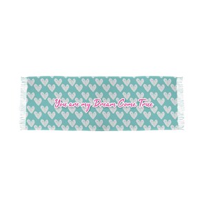 Op de afbeelding: Een rechthoekige turquoise deken met een wit hartpatroon en franjes aan de uiteinden. De zin "You are my Dream Come True" staat in roze letters in het midden.