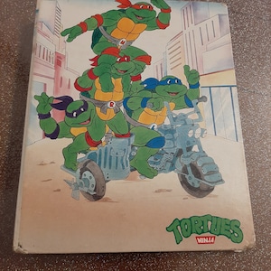 Könnte beinhalten: Ein Vintage-Buchcover mit vier Teenage Mutant Ninja Turtles, die ein Motorrad fahren. Das Cover ist weiß mit einem roten und grünen Titel "TORTUES NINJA".