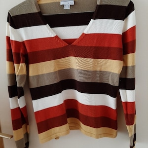 May include: A striped long-sleeved sweater with a v-neck. The sweater has alternating stripes of brown, white, red, and beige.
