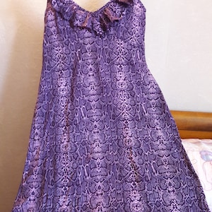 Peut inclure: Une robe sans manches violette à imprimé serpent et un col à volants.