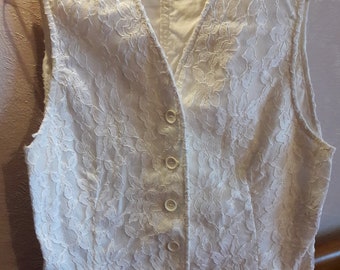 Peut inclure: Gilet en dentelle ivoire avec un col en V et cinq boutons. Le gilet sans manches est suspendu à un cintre en métal. Le motif floral en dentelle recouvre tout le gilet.