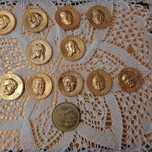 Peut inclure: Une collection de 10 pièces rondes dorées avec des portraits de personnages historiques. Les pièces sont disposées en cercle sur une dentelle blanche. Les pièces sont toutes de la même taille et ont un bord surélevé.