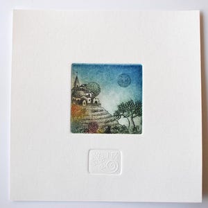 May include: A small, square art print featuring a whimsical landscape with a village on a hill, trees, and a moon in a blue sky. The print is set on a white background with a textured, embossed design.