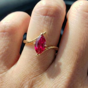 May include: A gold ring featuring a marquise-cut, vibrant red gemstone. The ring's band curves gracefully around the stone, creating a delicate and elegant design. The gemstone is the focal point, showcasing its rich color and shape.