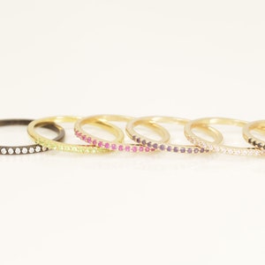 May include: A set of eight gold rings with a single row of small gemstones. The rings are stacked on top of each other, with the gemstones creating a rainbow effect. The rings are made of gold and have a polished finish.