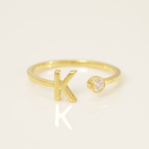 Puede incluir: Un anillo de oro con una sola letra 'K' y una pequeña piedra transparente.
