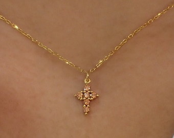 May include: A gold chain necklace with a small cross pendant adorned with tiny pink gemstones.