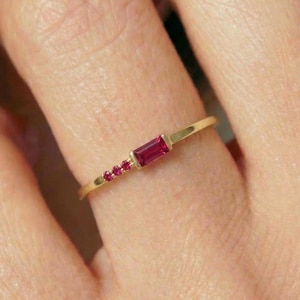 May include: A slender gold ring with a rectangular ruby and three smaller rubies. The ring's thin gold band complements the vibrant red gemstones. The design is minimalist and elegant, suitable for everyday wear. The gemstones are a vivid red.