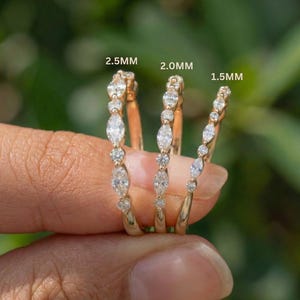Op de afbeelding: Drie gouden ringen met heldere edelstenen. De ringen zijn gemarkeerd met 2,5 mm, 2,0 mm en 1,5 mm. De edelstenen zijn een mix van ronde en marquise slijpvormen. De ringen worden tegen een vage groene achtergrond gehouden.