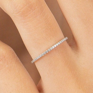 May include: A thin silver band ring with a row of small clear diamonds set around the entire band.