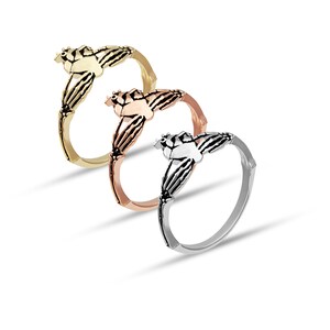 Puede incluir: Tres anillos de Claddagh en oro, oro rosa y plata. Cada anillo presenta un coraz&oacute;n sostenido por dos manos, coronado por una corona. Los anillos se exhiben sobre un fondo blanco, mostrando su intrincado dise&ntilde;o y acabados met&aacute;licos.